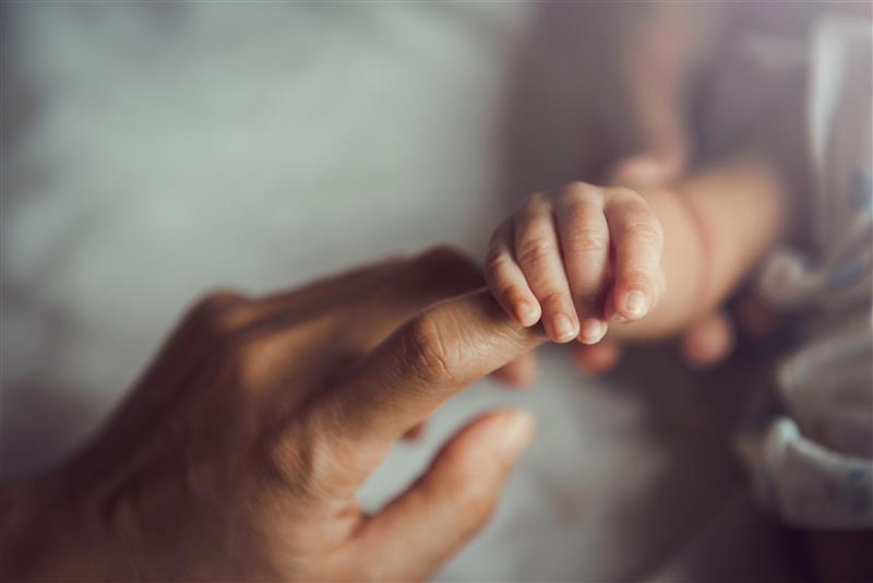 Close up of baby's hand grasping adult's finger