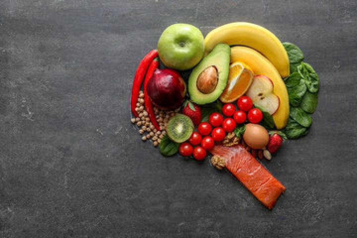 Image pf apples, bananas, avocado, nuts, cherry tomatoes, and a piece of salmon in an organized pile on a dark coloured table