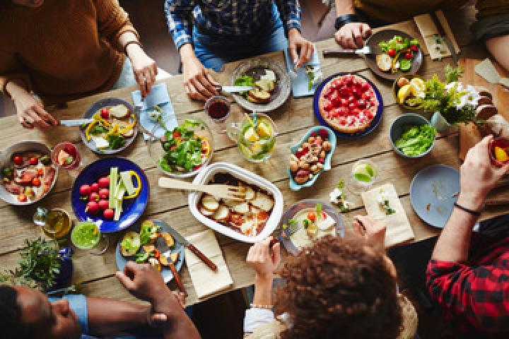 Bird eye view image of people sitting around a wooden table filled with various cooked food dishes